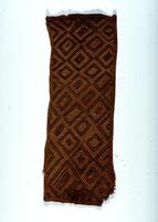 Brown panel with hemmed edges consisting of repetitive diamond pattern with tan and brown lines. The bottom right portion of the panel is frayed. 