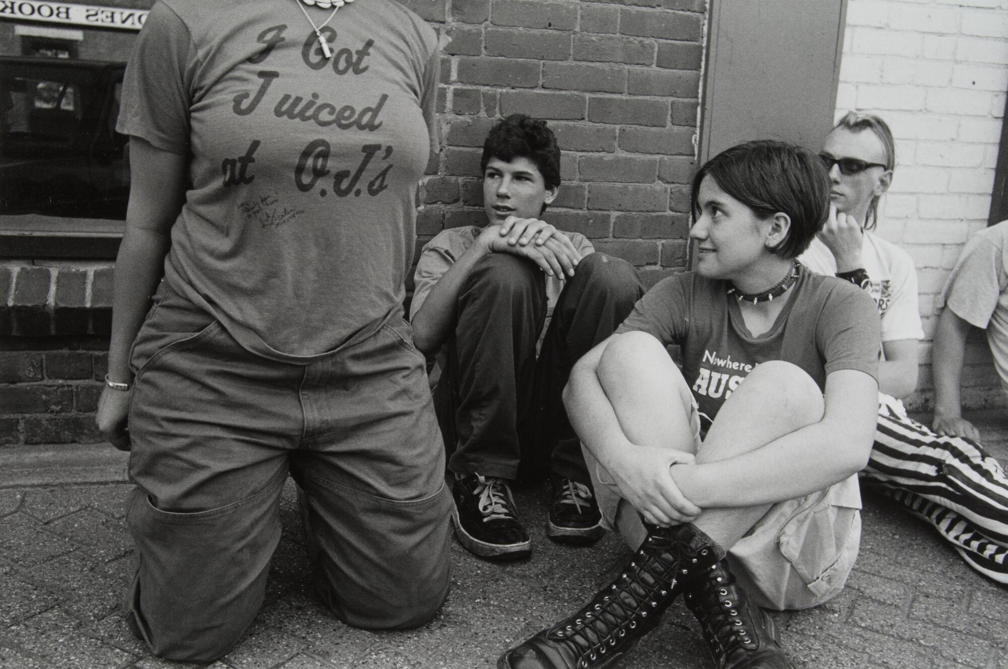 A girl kneeling with a &quot;I Just Got Juiced at O.J.&#39;s&quot; shirt on, another girl wearing combat boots.