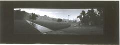This photograph depicts a panoramic view of two paths running through a suburban park. In the distance a couple of figures stroll by trees.