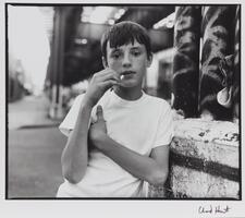 Young boy with cigarette in hand, drawn next to his mouth. The other hand is across his body and he is wearing a white t-shirt.