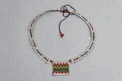 Beaded necklace with square beaded patch in the middle. Tie closure with long black threads with beads on the end. Triangular detail on sides of necklace. Chevron detail on patch. White, blue, red, green, yellow and black beads.