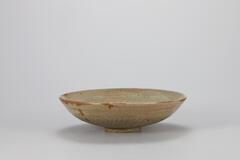 It has a relatively wide mouth for its height and slighly surving sides. Originally, this tpye of bowl was first produced in celadon in the late Goryeo period and was made in large numbers in buncheong ware during the early Joseon period. The foot is shallow and roughly trimmed.<br />
<br />
Many of densely decorated buncheong wares, with the stamped technique, were produced for uses in government offices in the 15th century. The interior wall and base of the dish are decorated with stamped designs of scrolls and chrysanthemum bands, and a chrysanthemum, respectively, while on the exterior wall is inlaid with lutus petals. Four spur marks are left on the inner base, and sand is adhered to the entire rim of the foot, which evidences that this piece was placed on the floor during firing. The glaze was fused well and made a glossy surface.<br />
[Korean Collection, University of Michigan Museum of Art (2014) p.148]