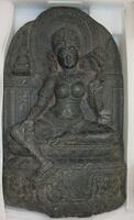 Black schist carved in the relief of Green Tara, a guide and saviouress on the Buddhist path to enlightenment.  She holds two lotuses, one open and one closed and makes the gesture of gift-giving with her palm facing outwards, towards the devotee.