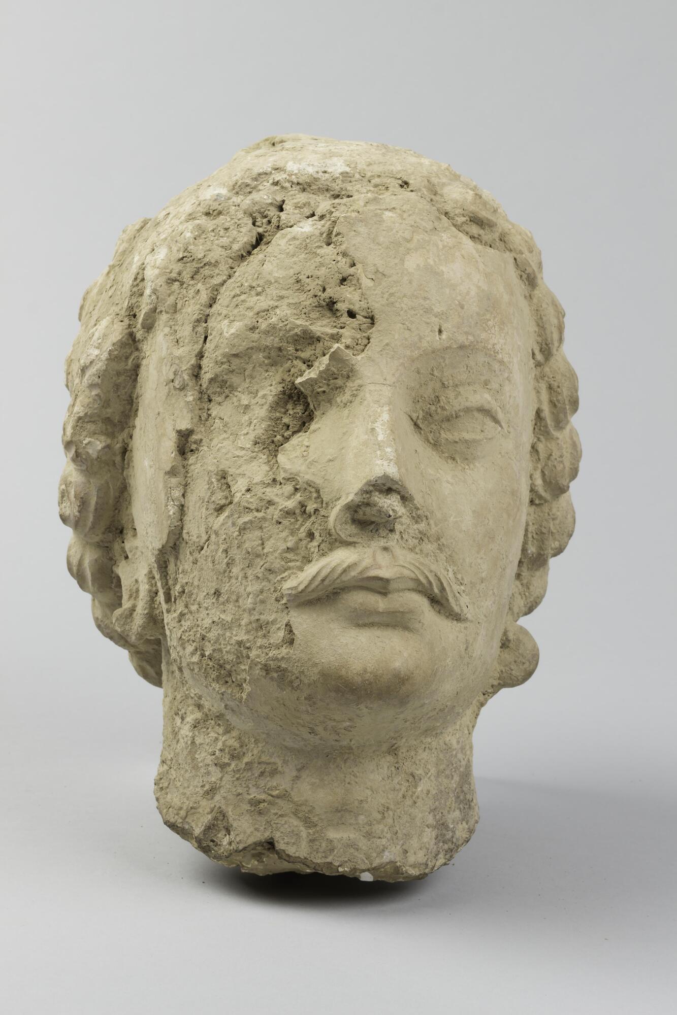 This head of a male figure with curly hair and a mustache would once have been part of a large stucco sculpture group. Part of the stucco has flaked away from the right-hand side of the face.