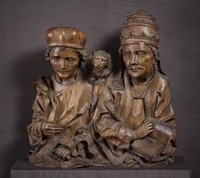 This pair of finely carved bust-length figures depicts two men in ecclesiastical garb. On the right appears an older figure who wears elaborate vestments and a papal tiara with a book in his left hand. His deeply lined and wrinkled face conveys a patient wisdom and authority as he stares directly ahead. His more youthful companion, dressed in a simpler collared robe and brimless cap, glances introspectively aside. He grasps an unfurled scroll in his left hand and a diminutive lion stares out from its perch on his left shoulder.