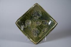 Green square shape plate with four corners of the plate curving upward. There are ten rough irregular shell shaped pattern in the center.