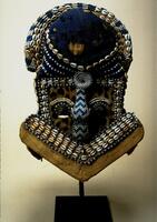 Mask of a human figure. Embellished with presitious materials: dyed cloth, leopard skin, cowry shells, glass beads.