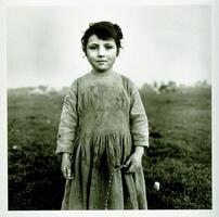 This photograph depicts a young girl standing in a grassy field wearing a stained and dirty dress.