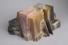A bronze, multi-colored work that has two triangles that form an entrance way on one side.