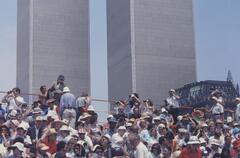 People seated on a grandstand looking at a parade passing by. The Twin Towers are in the background with clear skies.