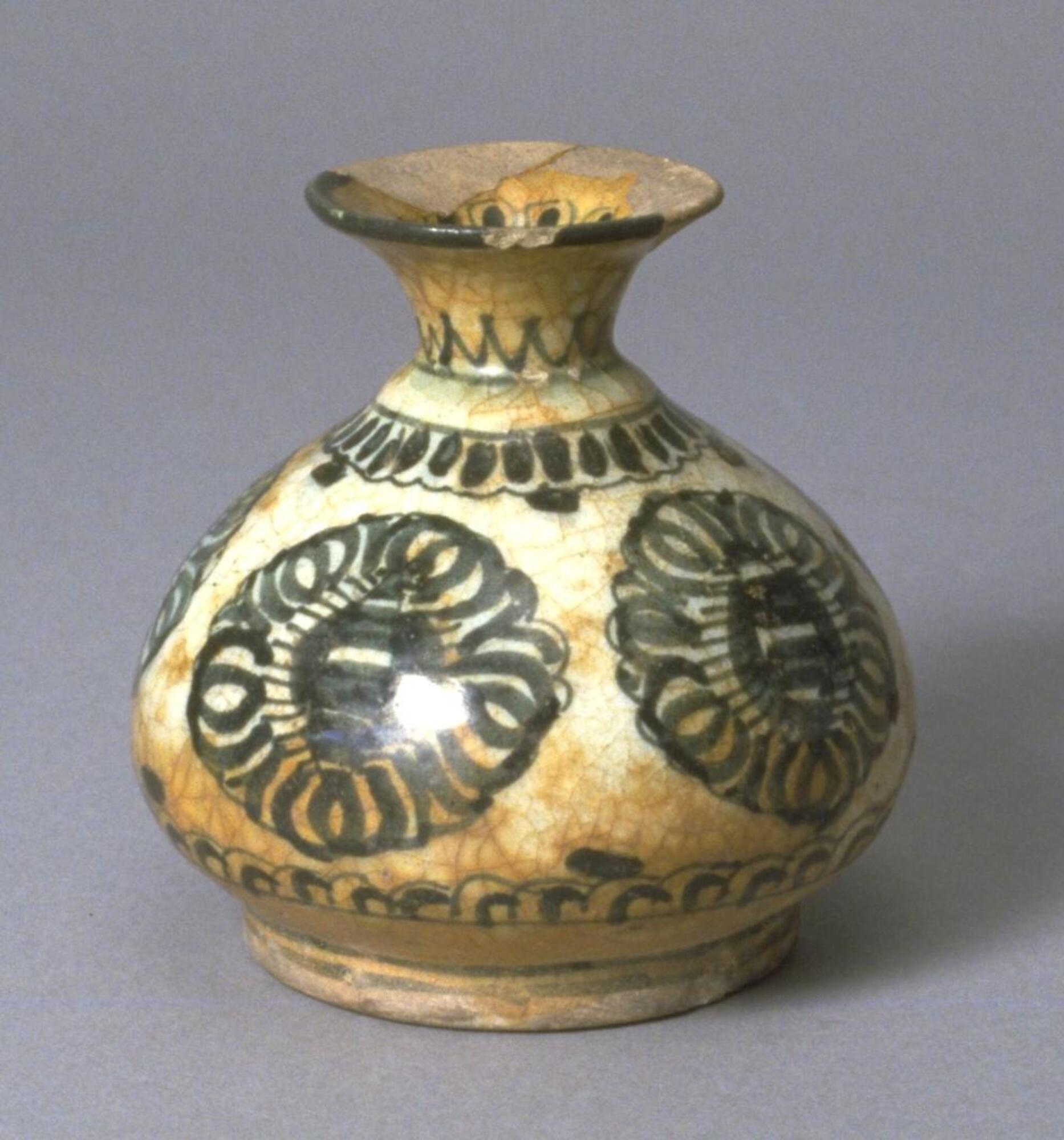 The unglazed ewer consists of two parts: a bulbous body with narrow, well-defined foot ring and short columnar neck; and a spout joined in the form of an anmial's head. A handle extends from the base of the head to the shoulder of the body. Around the upper part of the body runs an Arabic verse in Naskhi script. The moulded relief inscription is set against a background of floral scrolls. The meter is Tawil: (translated) Behold, poverty hopes for wealth, while wealth fears poverty." The verse appears in the 'Iqd al-Farid, compiled by Ibn 'Abd Rabbihi, who attributes it to 'Ali. The column above the body narrows to form a shoulder, on which the head has been set. The head is a cone, the narrow end of which serves as the animal's nose and has a small hole for pouring out the contents of the ewer. Over the base of the cone jut two pointed ears. Two loops are fastened below them to the shoulder of the neck. Small discs, serving as eyes, have been applied in the front of the ears. The hole for insertion of the liq