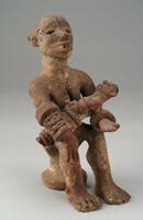 Seated female figure holding a child on her lap. The figure has a bracelet on each wrist and a pattern of incised lines on the chest and neck. The face also has scarification marks along the forehead, nose, and on each side of the eyes. 