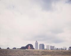 In the foreground of the photograph, a man sits atop a hill facing away from the camera towards a downtown skyline.