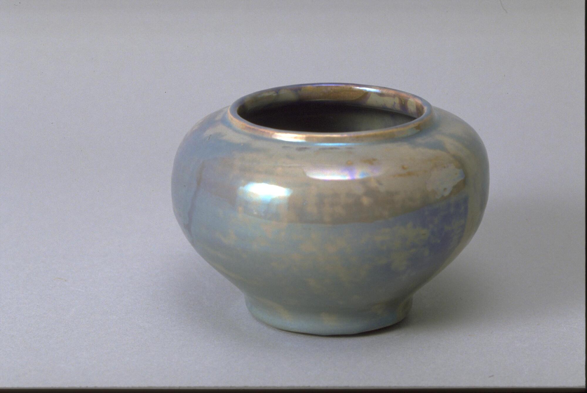 Footed vessel with round body, small lip and wide mouth covered in iridescent cracked gray-ish blue glaze