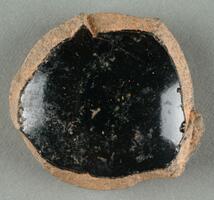 A curved, roughly round-shaped shard with black glaze. Broken edges expose a brown ceramic body.