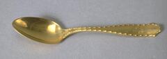 Gold spoon with thin handle that widens at the end with egg-and-dart-like motif along edges