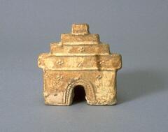 A miniature stove with arched doorway to a square firebox and stepped rear wall.  There is a round pot on top of a burner, and it is covered in a straw-colored glaze.
