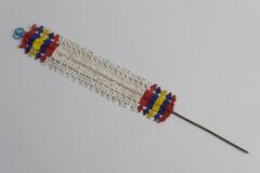 Beaded Jewlery with rectangular piece of metal wire extended from center. White beaded center section with red, blue and yellow stripe beaded end sections. Light blue loops at top. Beaded lattice designs at edges.