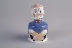 An inkwell made with porcelain has a cylinder shape body. The body is painted with drawings of a man in blue suit, sitting with his legs crossed in front; and the man's head is the lid cover/