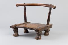 A small wooden chair with four rounded posts and an arched wooden bar on the back. There are carved triangle designs on the seat and finishing nails appear to be decorative.