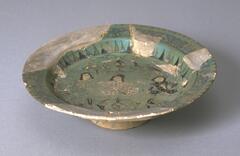 <br />
This <em>Mina'i </em>plate features seated figures of royalty, probably princes and/or princesses, along with two attendants and birds. There is a stylized inscription on the exterior. The glazed plate features turquoise, cobalt, black, white and brown-red coloring. It is likely a provincial or late <em>Mina'i  </em>style plate from the Seljuk period.<br />
 