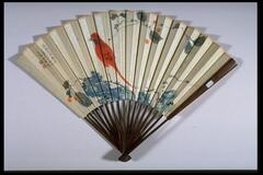 This is a folding fan with showing a small house behind a hill on its front side. The house has three different trees on the right side. Text runs vertically along the fan on the far left. The reverse of the fan shows a red bird perched on a small branch with redish cherries and blue flowers or leaves behind. Another small branch is above with text on the far left. 