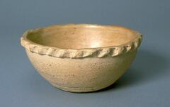 Beige bowl, wider at the top, with a rim formed in a braided pattern.