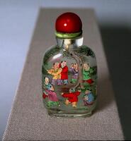 A glass snuff bottle with a scene of boys playing around a tree. On top is a red stopper.