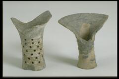 This black-gray earthenware, tall-stemmed pedestal vessel has a bowstring pattern around the body and a wide flaring rim on a narrow base. There is significant loss to the rim.  
