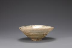 It has large-mouth and the wall slants toward the bottom in an almost straight line. It was deformed during firing.<br />
<br />
The inner and outer surfaces of this bowl are brushed with white slip. Traces of refractory spurs remain in five places on the inner base and the foot. The foot is glazed on the rim as well. This is a low-grade object with many iron-brown spots on both its inner and outer surfaces. A note from collector is adhered to the reverse side of the bowl, and it reads, &ldquo;19629, cor&eacute;e, Hak&eacute;me,&rdquo; &ldquo;朝鮮刷毛目, 三百年.&rdquo;<br />
[Korean Collection, University of Michigan Museum of Art (2014) p.156]