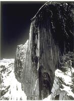 Photographed near the summit of a snowy mountian peak, this photograph depicts a steep cliff sloping down through the center of the frame.