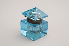 This is a blue crystal glass inkwell with a dark metal collar. The body has a cube shape with cut corners. The lid is a four-sided pyramid with cut corners.<br />