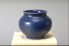 Ceramic vessel with round body wide mouth and slightly flared lip covered in a bright blue-gold iridescent glaze