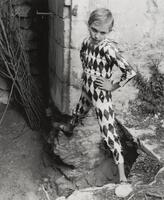 This portrait of a young boy in a harlequin costume shows him looking into the camera lens. He stands in the ruins of Arles, arms akimbo, balancing on the ruins of the foundation of a building. 