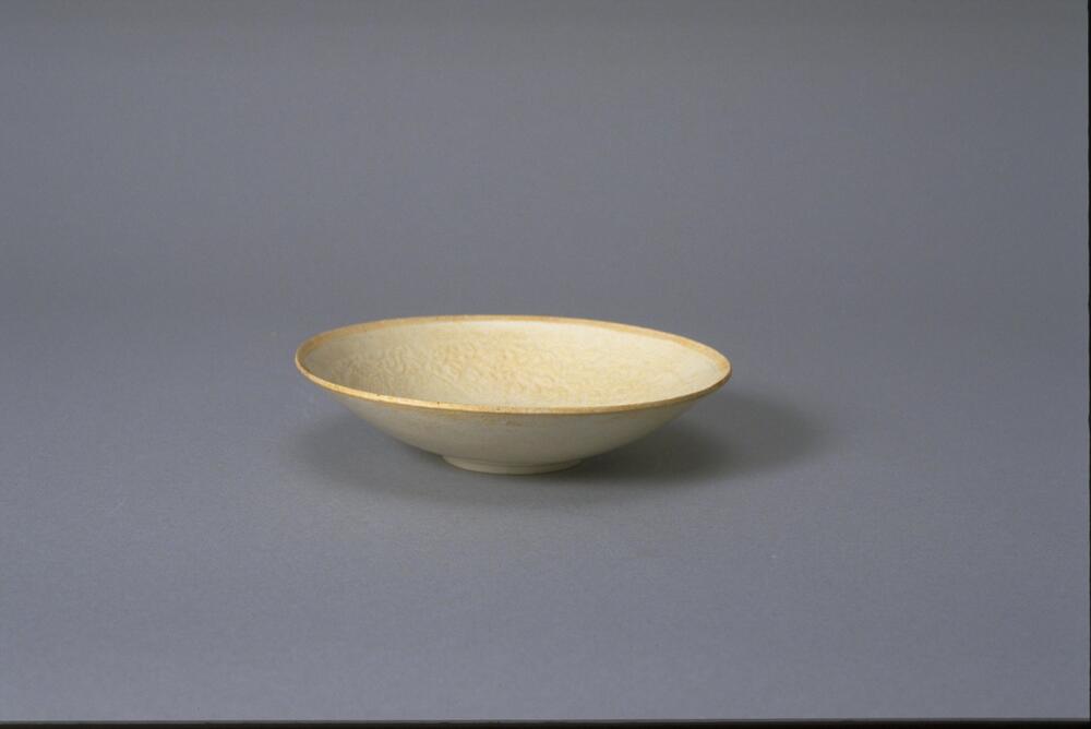 This thin porcelain conical bowl with direct rim on a footring has an interior with incised floral meander decoration. It is covered in a white glaze with bluish tinge and has an unglazed rim.