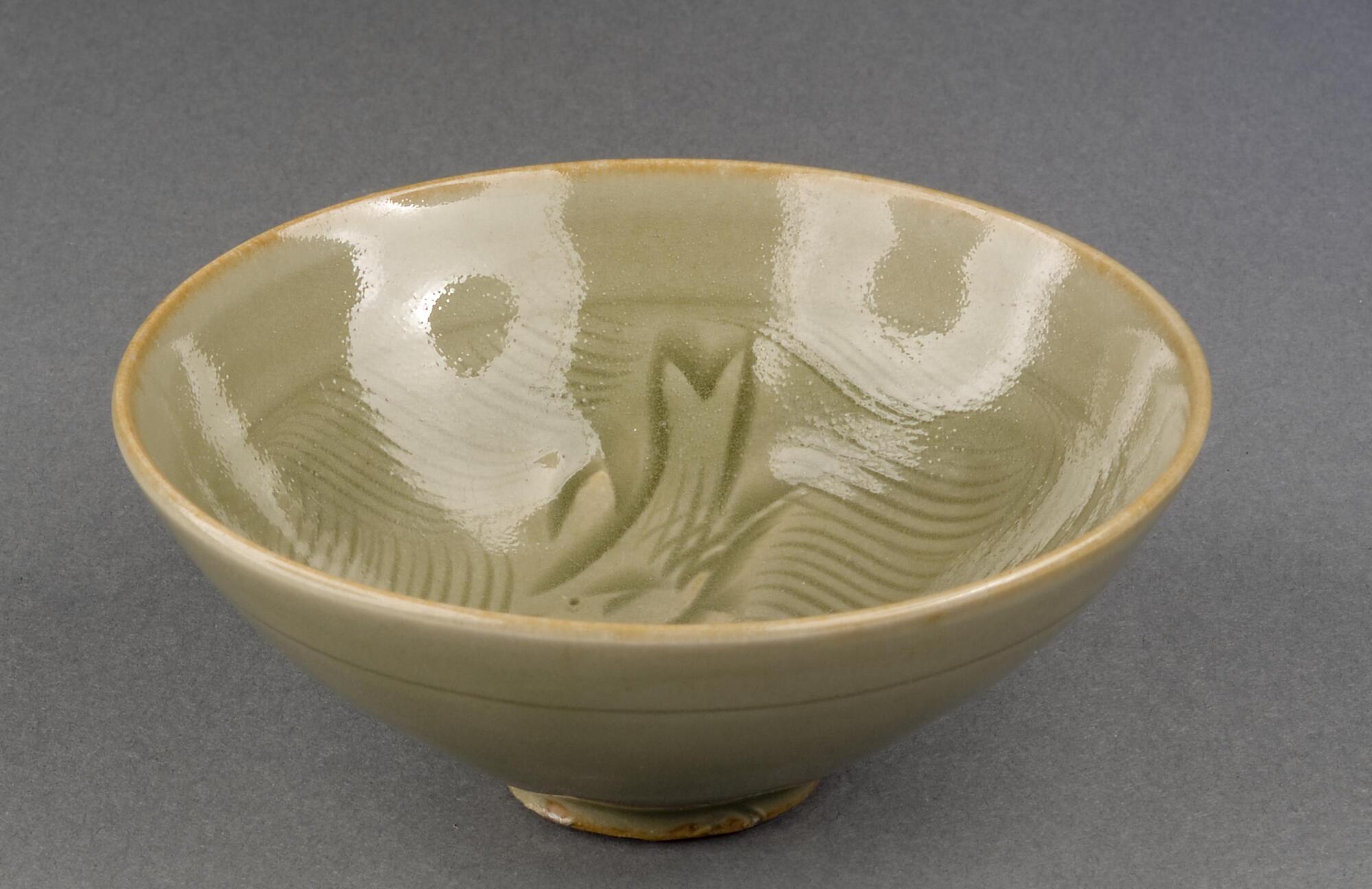 a northern celadon bowl of conical shape, incised with abstract depictions of fish and waves on interior, small ring foot