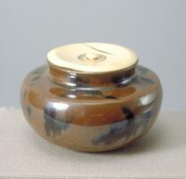 This squat tea caddy is decorated with brown glaze with splotches of black.  It is capped with a round ivory lid with a small circular knob-handle.