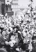 A child rides upon a man's shoulders amid a crowd of people holding flowering branches in their hands. 