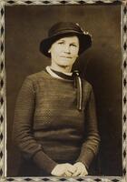A portrait of a woman wearing a long-sleeved sweater, neck scarf, and hat. The photograph has a decorative border.