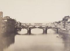 Picturesque scene of the Arno River in Florence, Italy. The image is of the river, directly looking at the length of the bridge. The buildings on either side are visible.