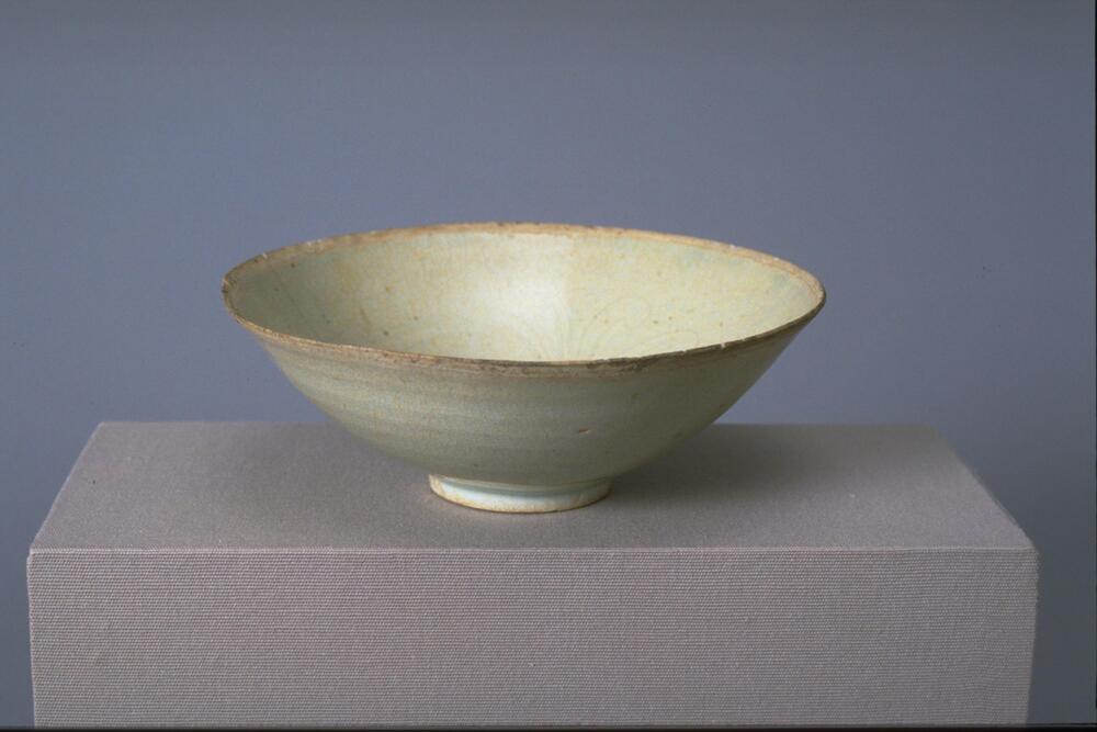 This thin porcelain conical bowl with direct rim on a footring has an interior with incised floral meander decoration. It is covered in a white glaze with a bluish tinge.