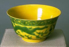 A tall chicken fat yellow bowl with green dragon design on a footing.