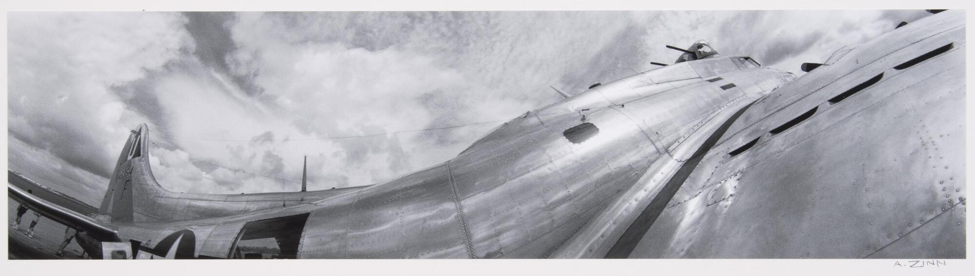 Wide angle view of the body of a silver plane and cloudy sky above.