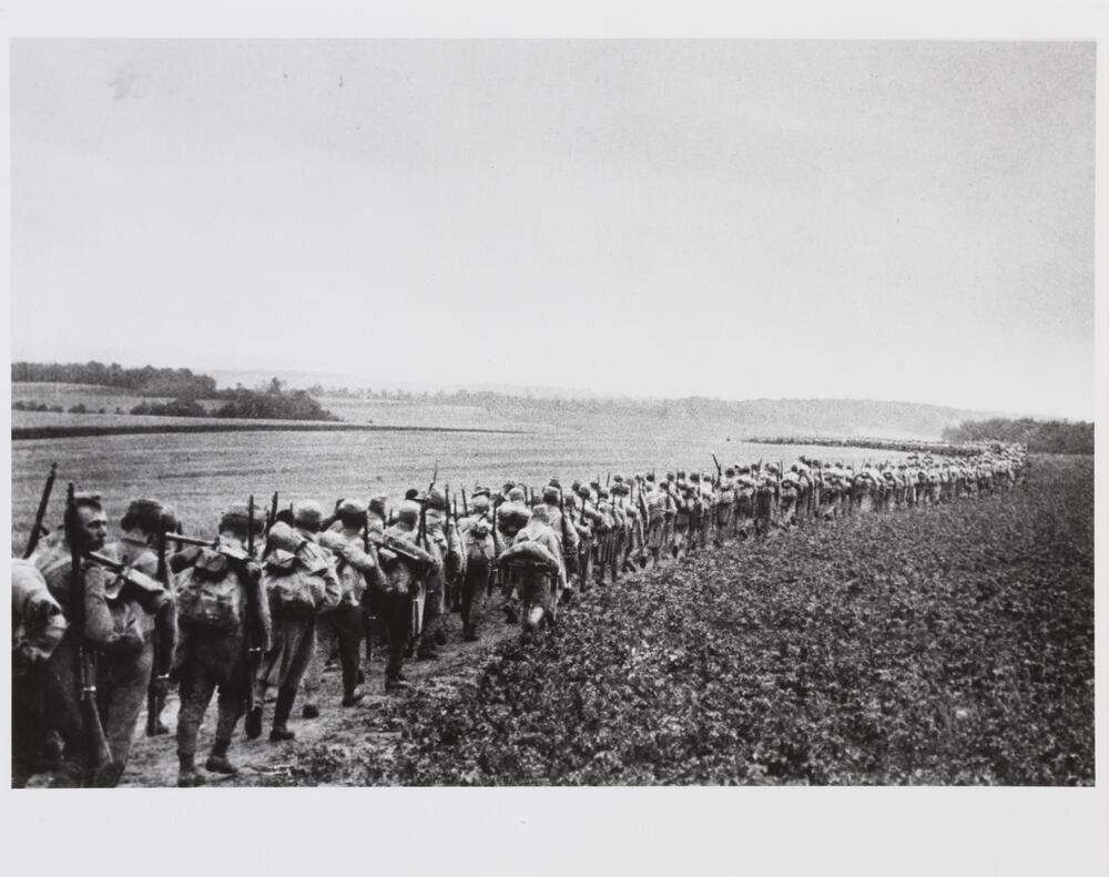 Photograph of a long procession of soldiers marching in a rural landscape.