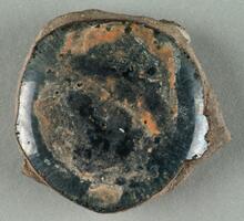 A curved, roughly round-shaped shard with black glaze and russet mottling. Broken edges expose a gray-brown ceramic body.