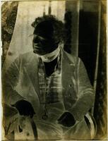 This photographic negative depicts an older man seated in an interior. His head is turned to the side and he wears a three-piece suit.