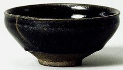 A deep, conical bowl on a straight foot ring, with subtle rim articulation. It is covered in a thickly applied dark iron-rich black glaze with silver-gray mottling. There is a stress crack from firing to rim and side. 