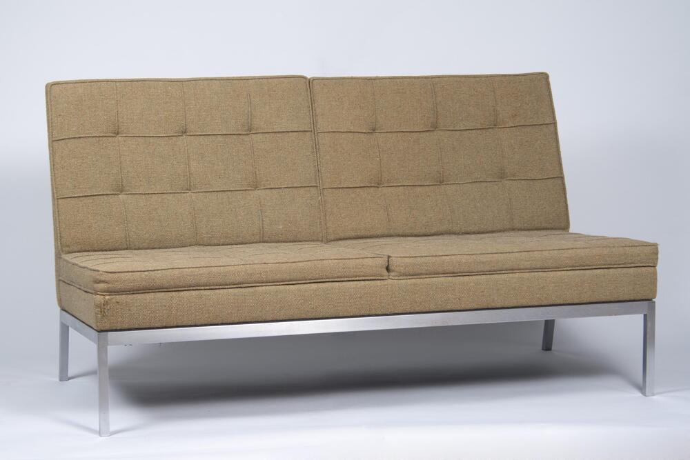 A two-seat settee upholstered in green/gold wool textile, attached to a metal frame of square tubular steel.