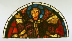 A lunette-shaped panel composed of red, blue, white, brownish purple and yellowish brown stained glass joined together by lead cames depicting a seraph. Four leafy fronds, taken from another medieval window, have been inserted here between the seraph's head and shoulders. The panel is the upper half of a roundel originally installed in the west rose window of Reims Cathedral.