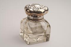 A square crystal inkwell with rounded sides and a star etched into the bottom of the base. The lid is sterling silver and monogrammed.